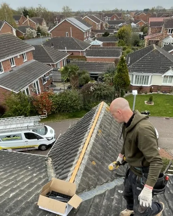 Roofer setting a new ridge on a grey tiled roof