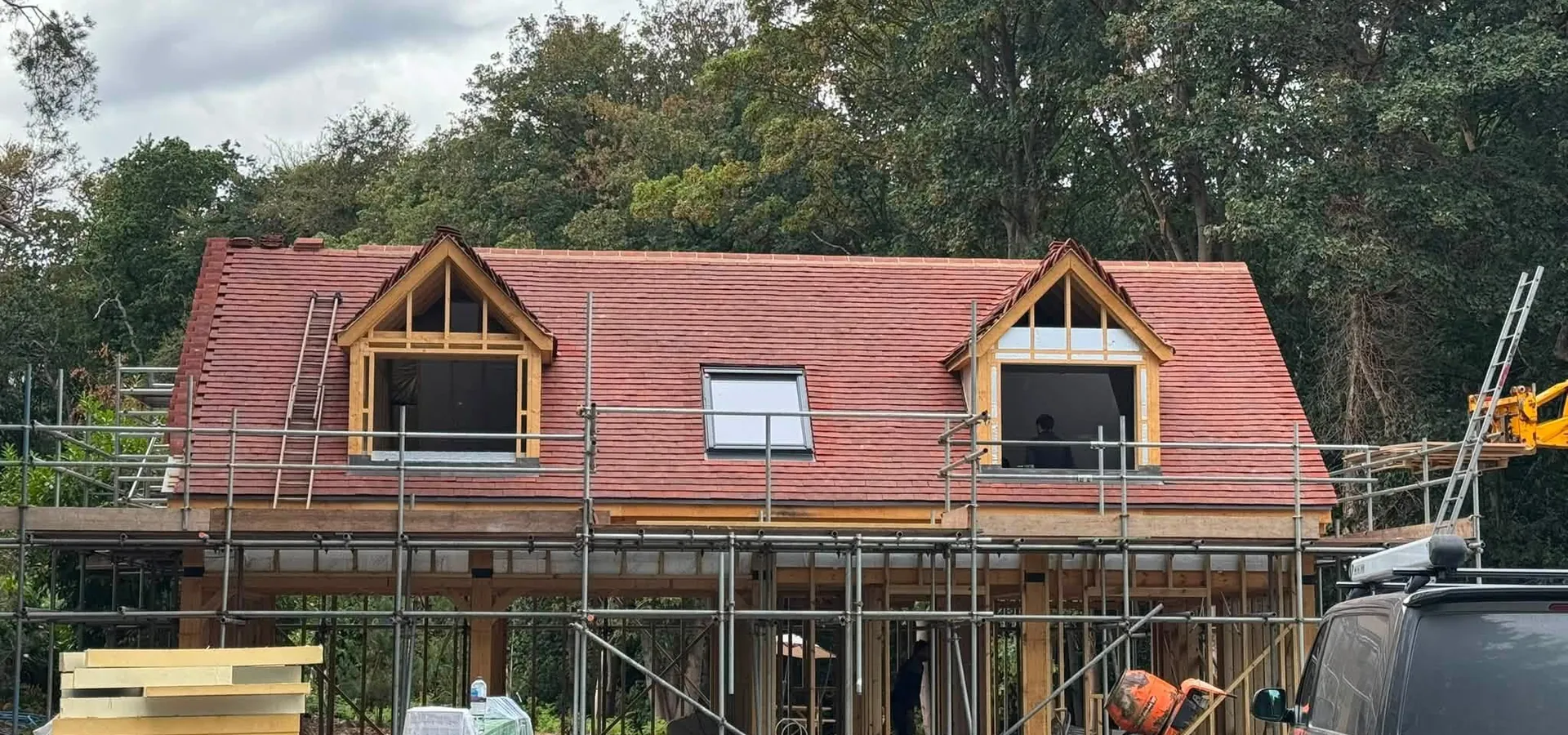 New red tiled roof with oak framed dormers and a roof window, under scaffolding
